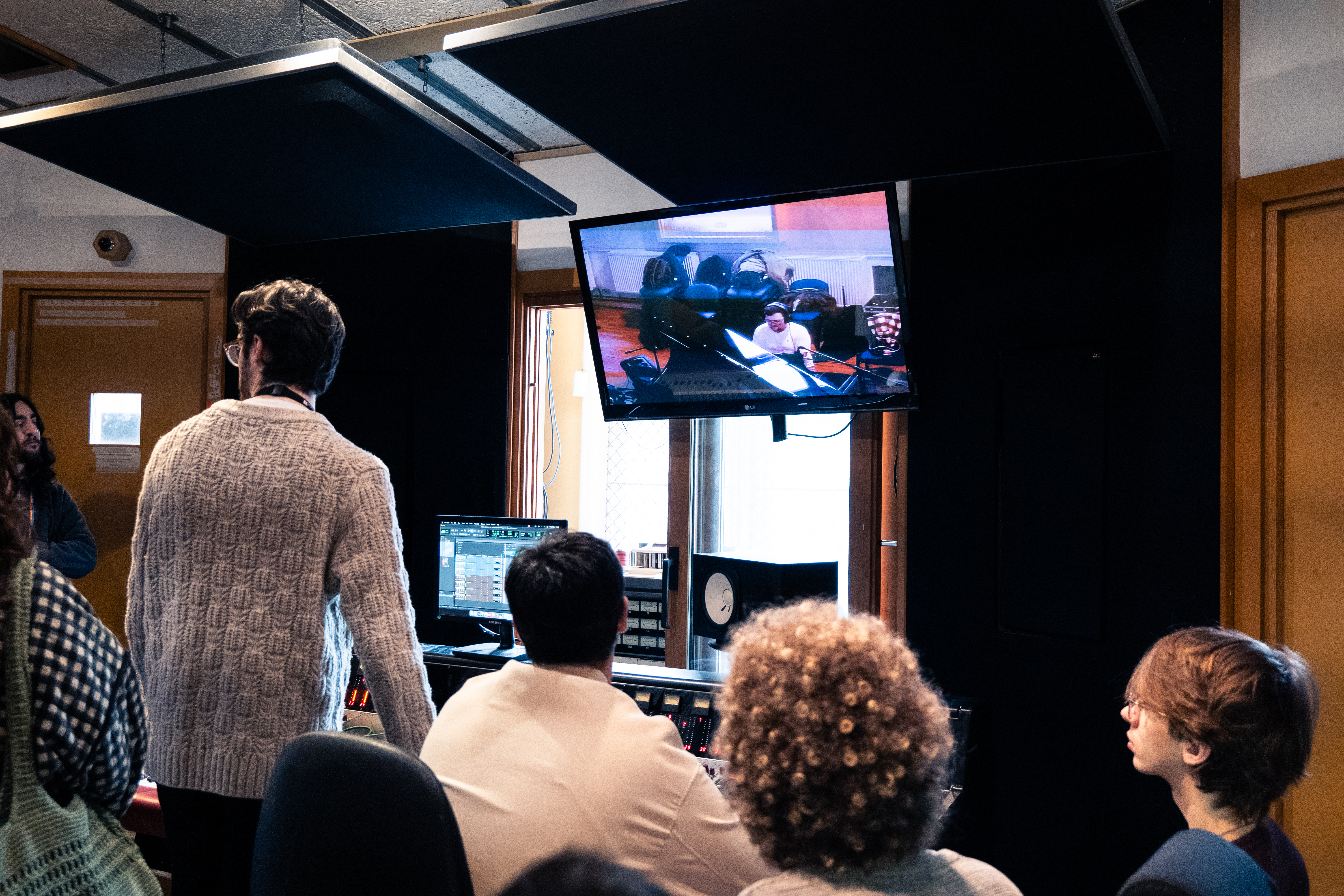 Stood in front of a mixing console, a video feed of a pianist above.